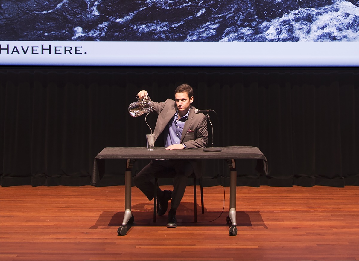 A wall mounted, framed image, of a man in a suit, staring at the camera from his seat on an empty stage